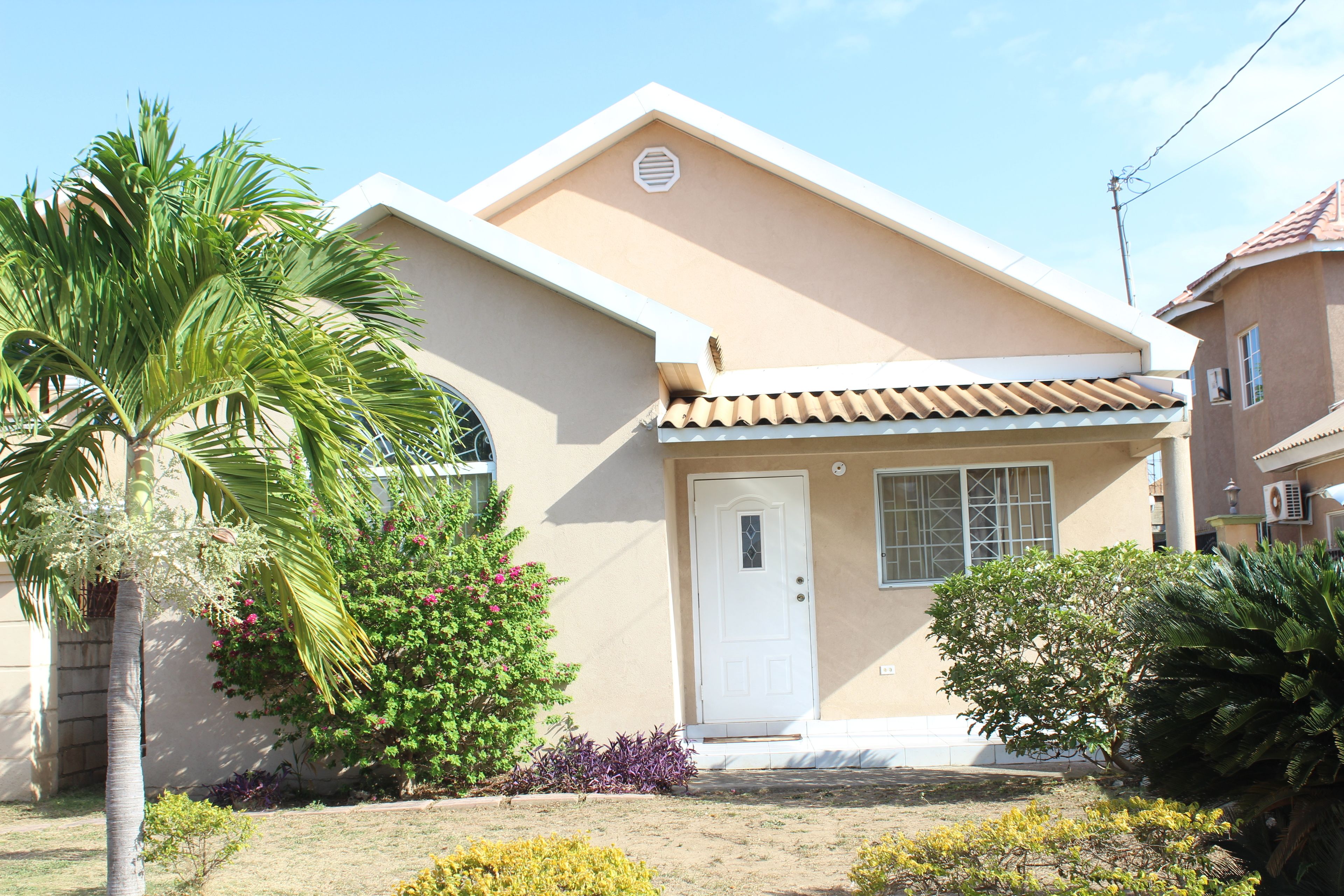 A single-story house with a beige exterior, a white door, and a tiled roof.