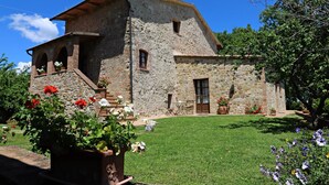 Une maison de campagne en pierre, dotée d’un toit en pente, d’un petit porche et d’un jardin bien entretenu où poussent des plantes à fleurs.
