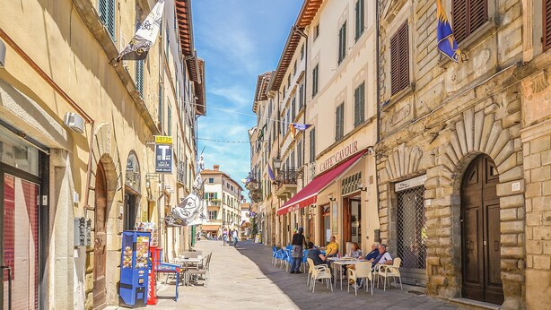 A narrow street lined with traditional buildings, outdoor seating for cafes, and a visible storefront with a red awning. - Beautiful home in Monte San Savino -AR- (Monte San Savino -AR-)
