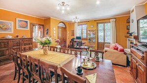 A dining area with a wooden table, chairs, and a vase of flowers. There is a television and a fireplace in the background. - Beautiful home in Monte San Savino -AR- (Monte San Savino -AR-)