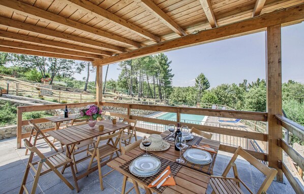 Une terrasse en bois avec une table dressée pour le repas, donnant sur une piscine et un paysage montagneux.
