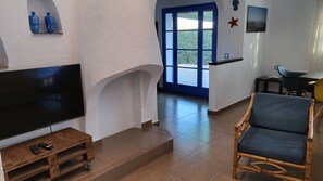 Un soggiorno con televisione, mobili in legno, una porta blu e vista sull'esterno.