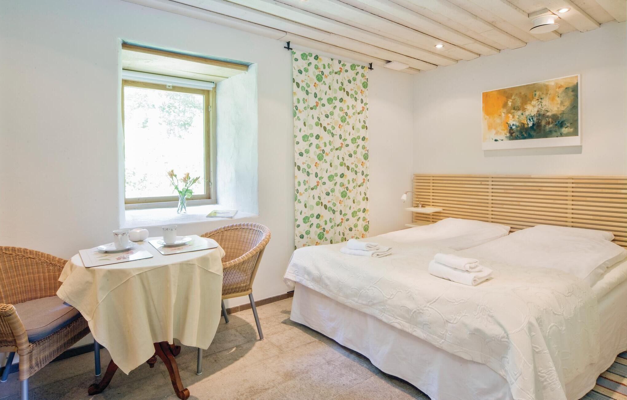 Quarto com cama, janela com vista, mesa com cadeira e um quadro na parede.
