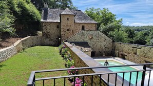 A stone building with a swimming pool, surrounded by a stone wall and lush greenery.