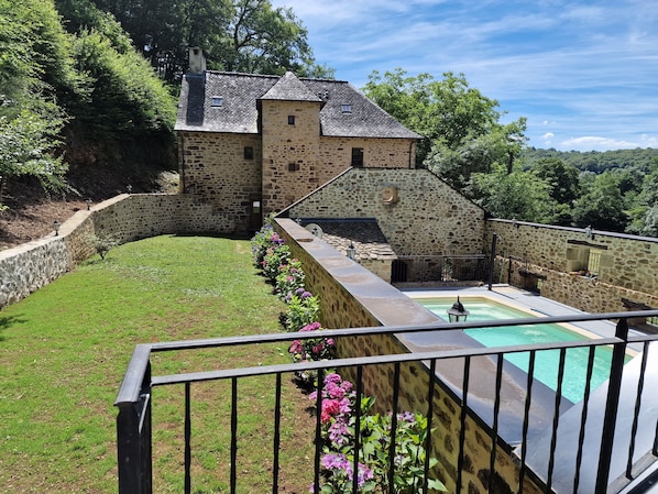 A stone building with a swimming pool, surrounded by a stone wall and lush greenery.