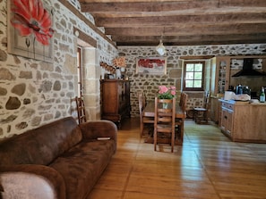 A rustic interior with a stone wall, wooden furniture, a wooden ceiling, and a kitchen area.