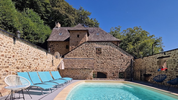 A stone building with a swimming pool, lounge chairs, and a stone wall.