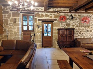 A rustic room with stone walls, a wooden door, a leather sofa, a wooden table, and a chandelier.