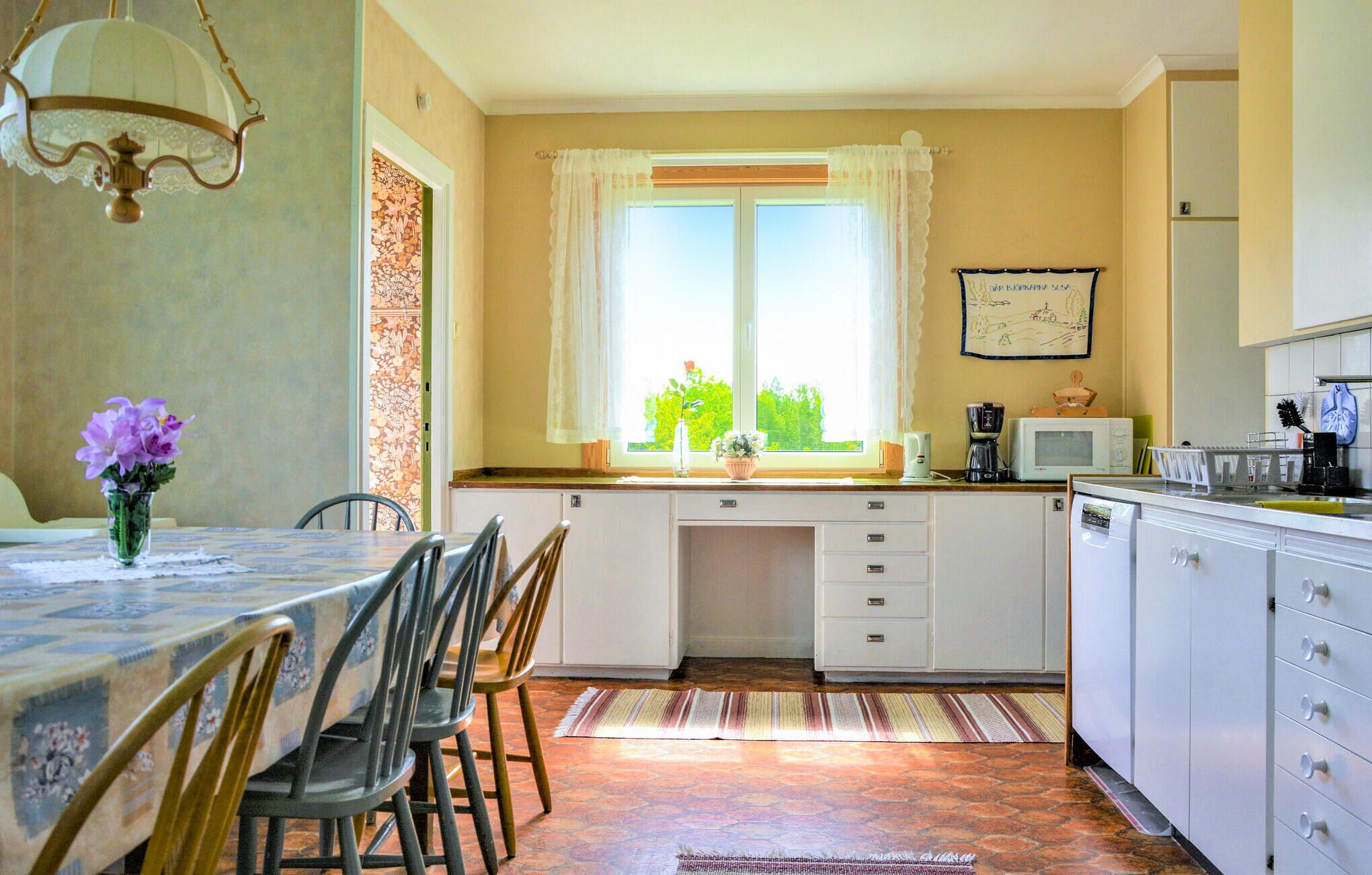 Eine Küche mit Essbereich, ausgestattet mit einem Tisch, Stühlen, einem Fenster mit Vorhängen und einem Kühlschrank.