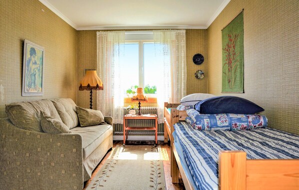 A cozy room with a sofa, a bed with a patterned bedspread, a small table with a lamp, and a window with curtains.