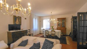 Una sala de estar con sofá, televisor, candelabro y comedor con mesa y sillas.