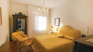 Habitación de hotel con una cama grande, una silla, un escritorio, un aparador, un candelabro, un espejo y una ventana con cortinas.