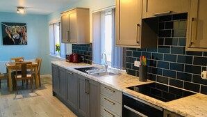 A modern kitchen with grey cabinets, a black tiled backsplash, a marble countertop, and stainless steel appliances.