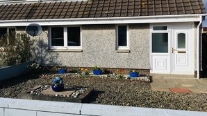 A two-story house with a tiled roof, a satellite dish, and a garden with pebbles and flowers.