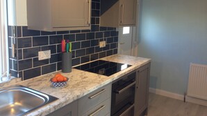 A kitchen with grey cabinets, black tiled backsplash, and a marble countertop.