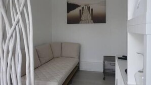Een minimalistische kamer met een witte bank, een schilderij van een brug en een klein tafeltje met een mandje.