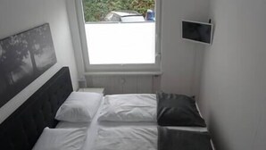 Een kleine kamer met een enkel bed, een raam, een flatscreen televisie en een hoofdbord.