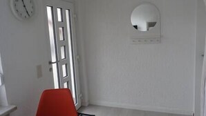 Een kamer met een deur, een klok en een ronde spiegel aan de muur.