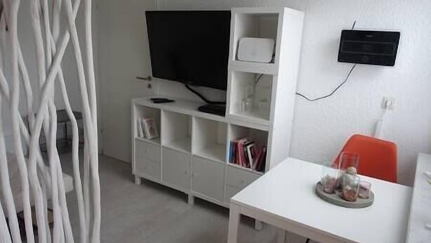Een kamer met een witte tv-standaard, een flatscreen televisie, een witte tafel met een dienblad en een rode stoel.