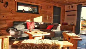 Interior acolhedor de uma cabana com parede de madeira, um sofá, uma mesa de centro e uma pequena mesa de madeira.