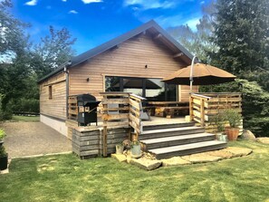 Une cabane en bois avec une véranda, un barbecue extérieur et un grand parasol.