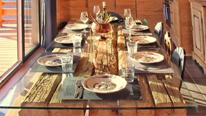 Uma mesa de jantar posta com pratos, copos e talheres, rodeada por armários de madeira e uma grande janela.