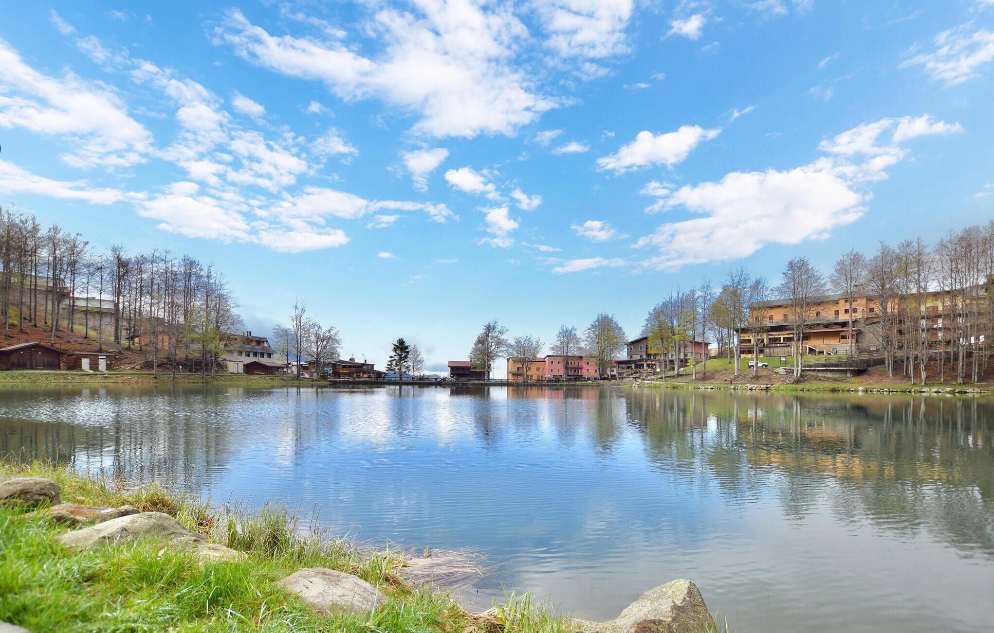 A serene lakeside view with buildings on both sides, reflecting the clear sky.