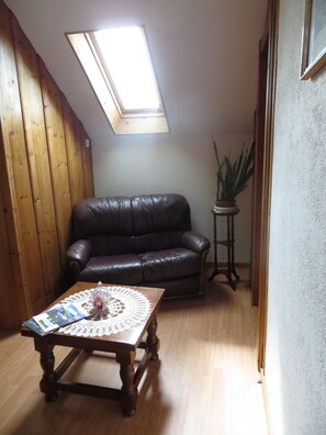 Una sala de estar con techo de madera, tragaluz, sofá de cuero, una mesa de centro con un encaje y una planta en maceta.