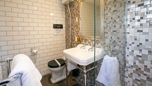Ein Badezimmer mit weißen Fliesen, einer Duschkabine aus Glas, einem weißen Waschbecken und einer Toilette mit schwarzem Sitz.