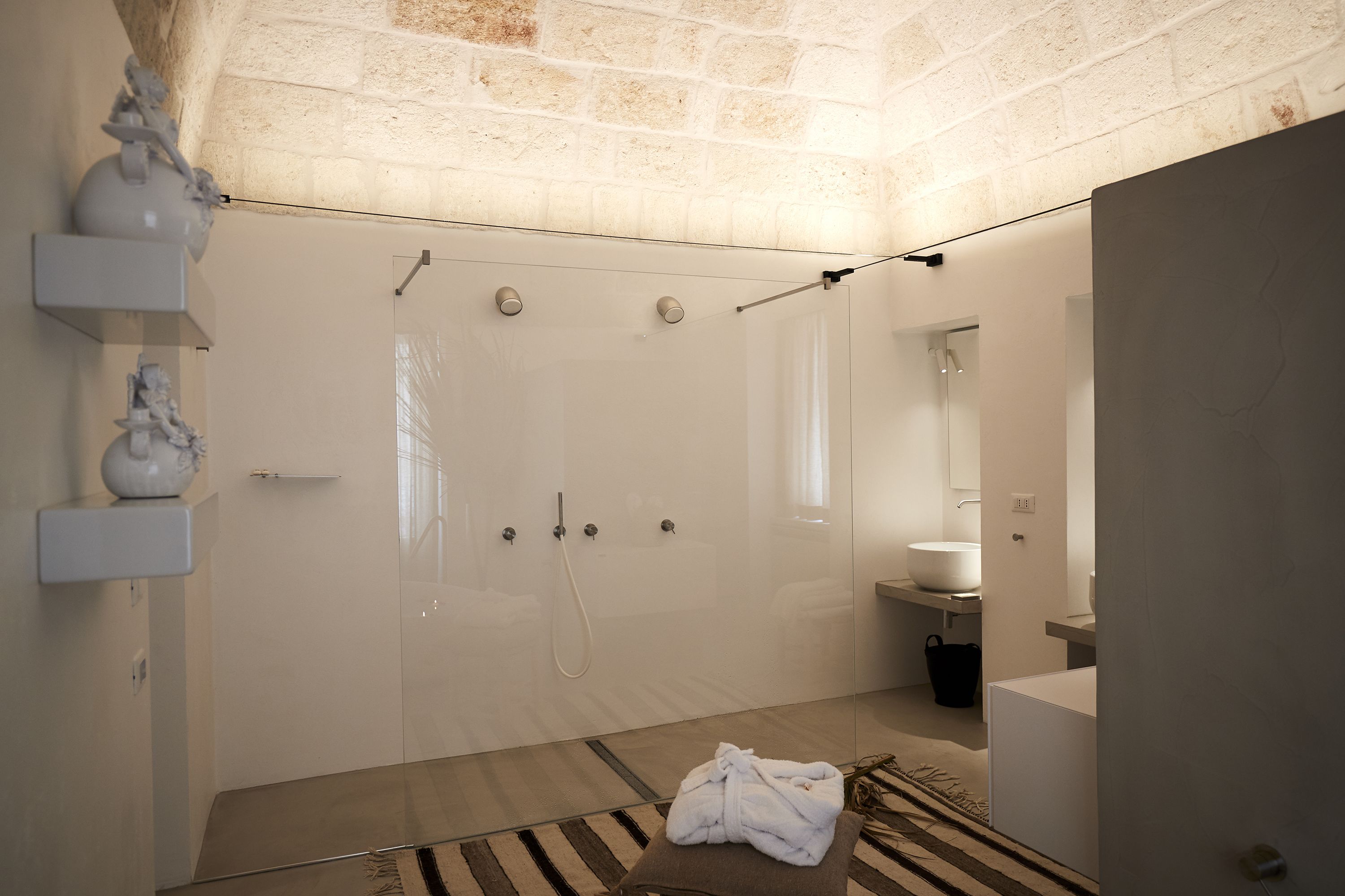 A modern bathroom with a glass-enclosed shower, a white sink, and a towel on the floor.