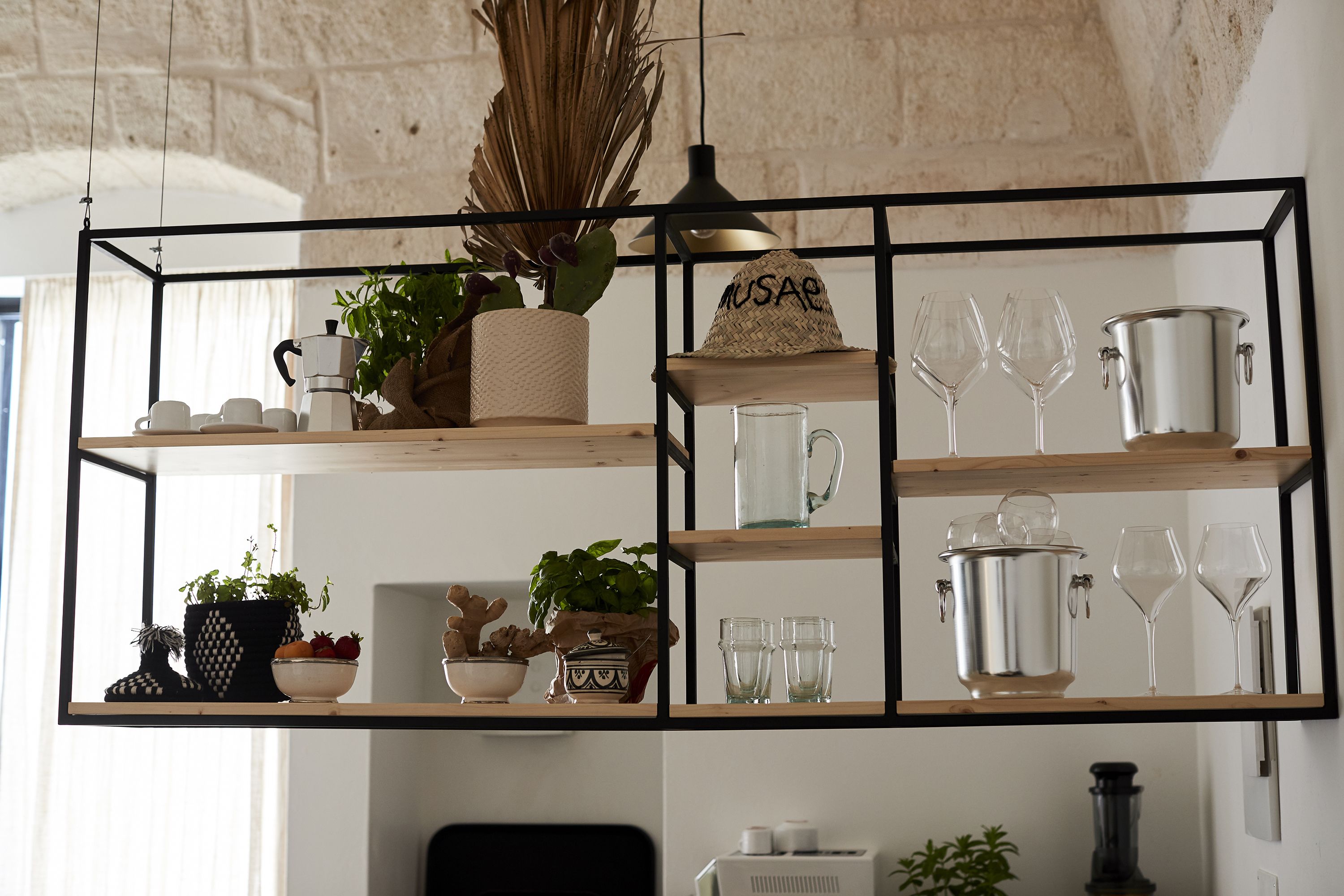 A wooden shelf unit with various kitchen items, including a coffee maker, pots, and glassware.