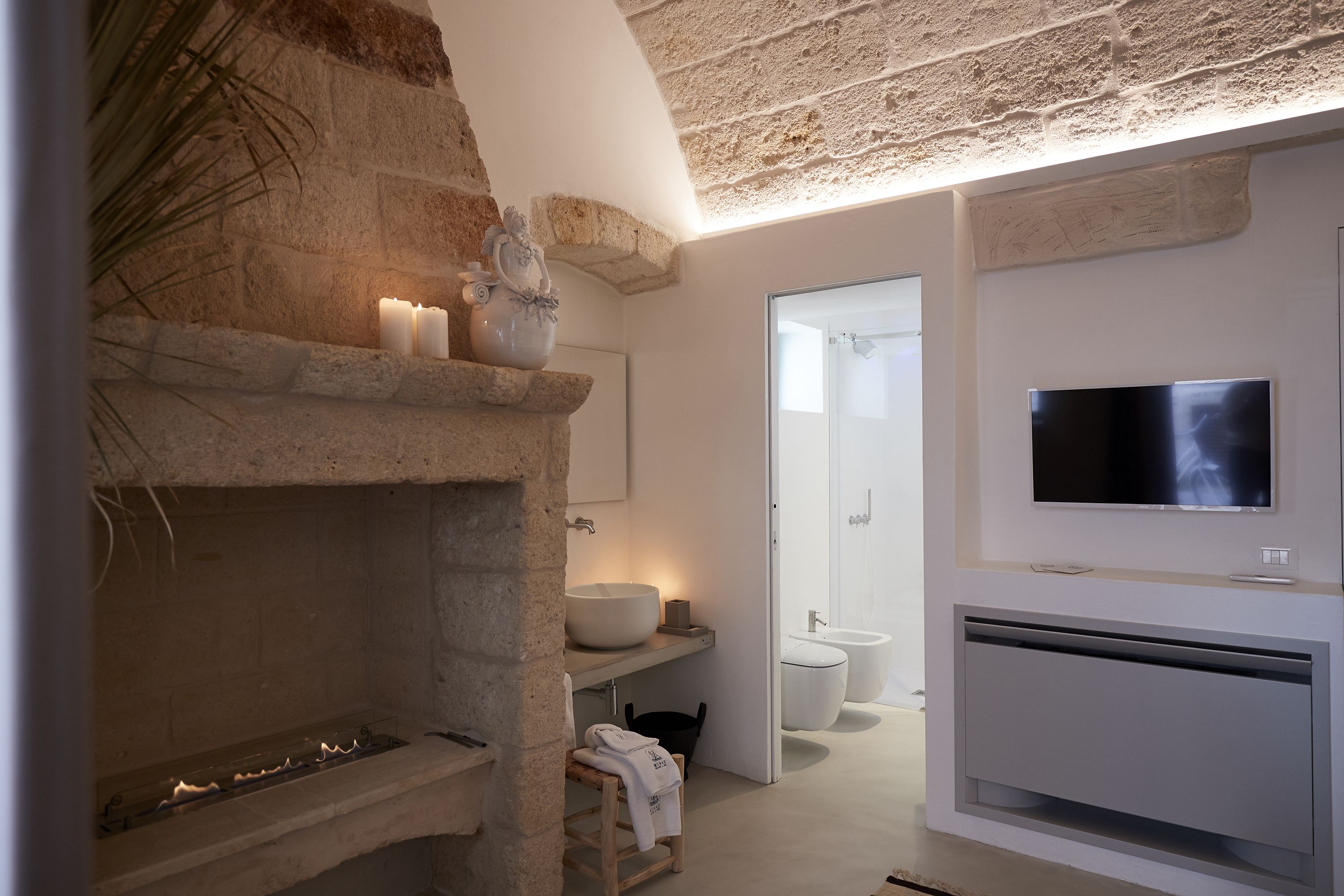Une salle de bain moderne avec une cheminée en pierre, un grand miroir, un téléviseur et un espace douche.