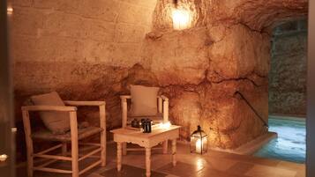 Una habitación de paredes de piedra con una mesa de madera, dos sillas, una vela y un farol.