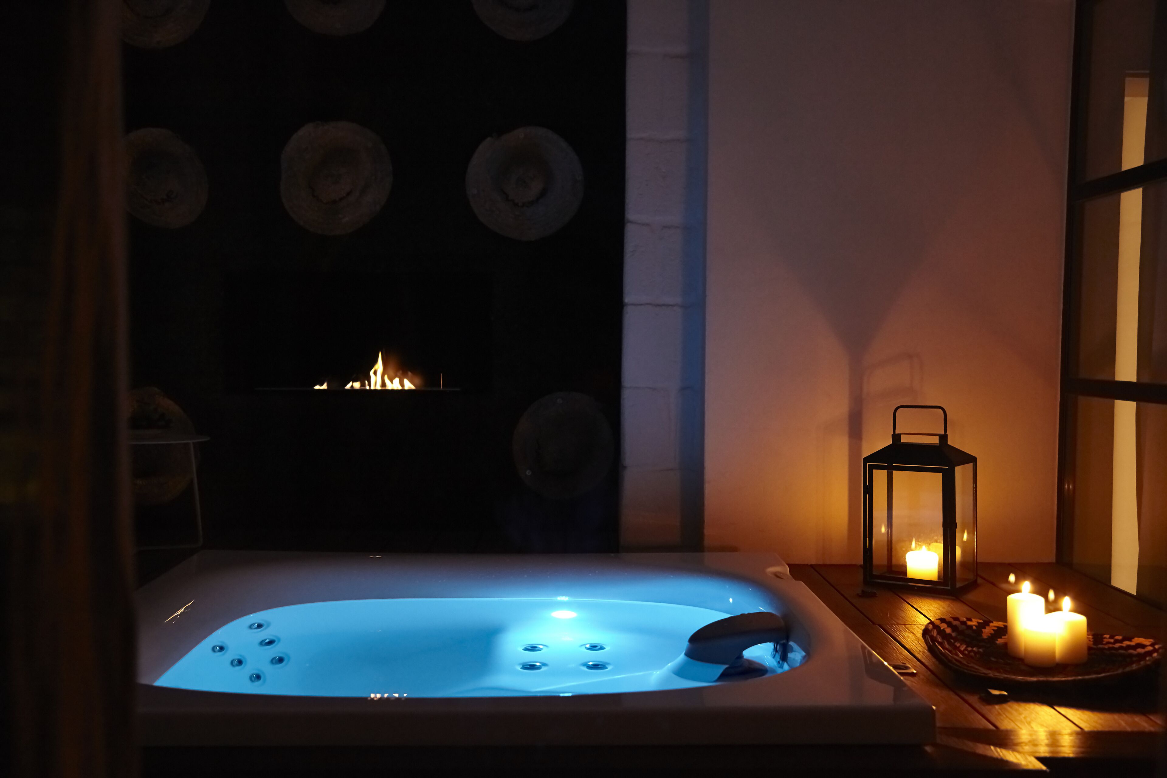 Een hottub met blauw licht, kaarsen en een lantaarn op een houten tafel.