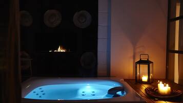 Een hottub met blauw licht, kaarsen en een lantaarn op een houten tafel.