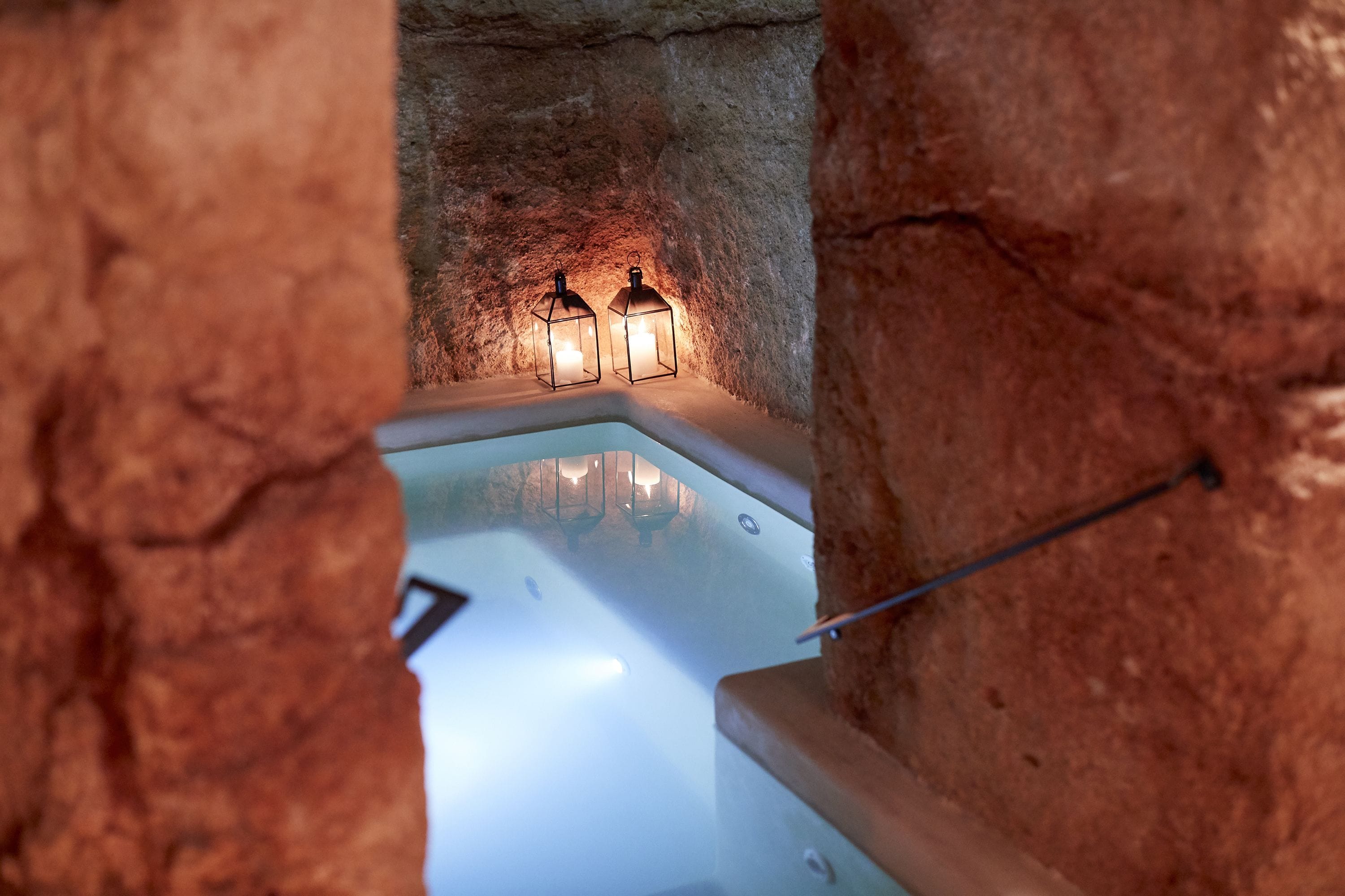 A spa area with a bathtub, two wall-mounted lanterns, and a stone wall.