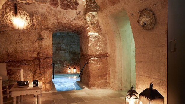 A stone-walled room with a pool, a wooden table with bowls, and two lanterns. - Musae Relais & Spa (Polignano a Mare)