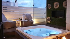 A hot tub with a TV mounted on the wall, a sofa, and a small table with candles. - Musae Relais & Spa (Polignano a Mare)