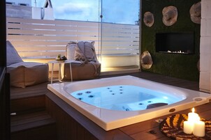 A hot tub with a TV mounted on the wall, a sofa, and a small table with candles.