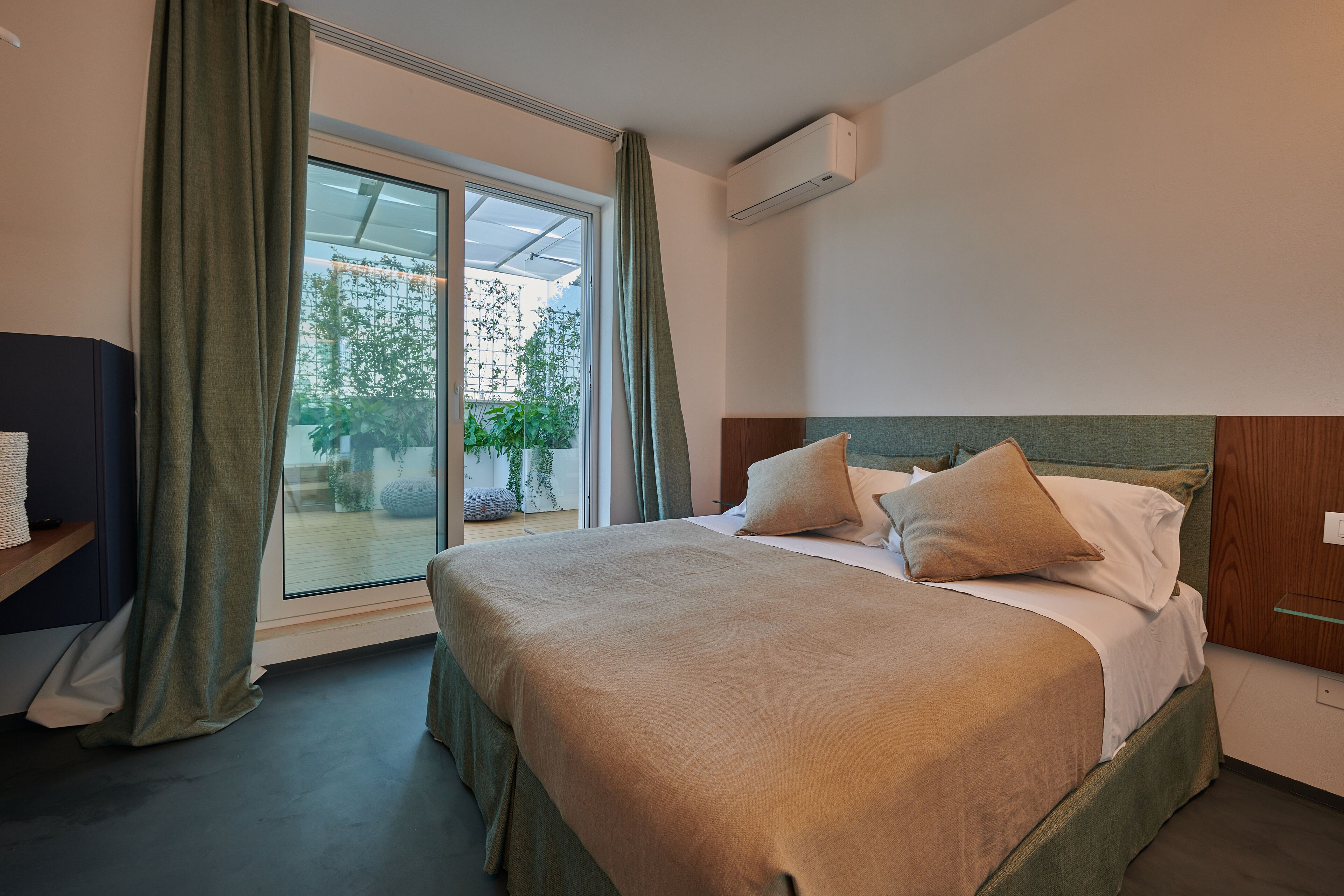 A hotel room with a large bed, a nightstand, a window with curtains, and an air conditioning unit on the wall.
