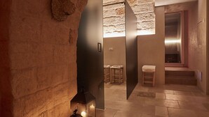 A modern interior with a stone wall, a wooden bench, and a small table. - Musae Relais & Spa (Polignano a Mare)