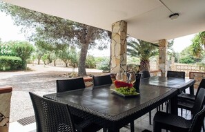 An outdoor dining area with a stone pillar, wicker chairs, and a table set with fruit. - Stunning House Between the Countryside and the Sea - Southern Sardinia CIN: IT111070C2000U0960 (Porto Pino (Sardegna))