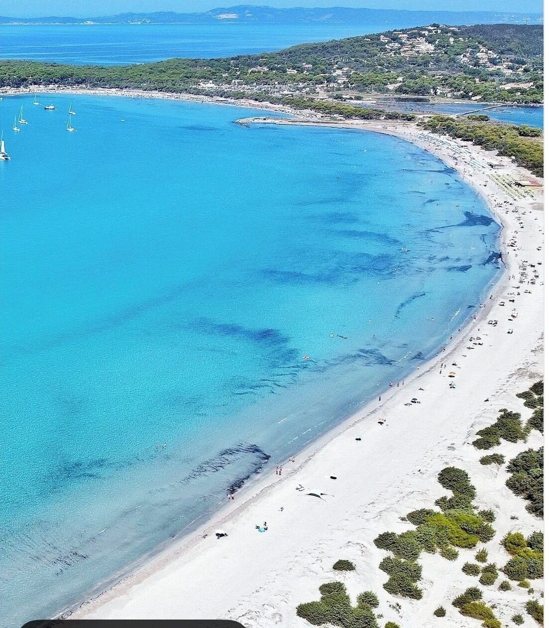 Una spiaggia costiera con acque blu cristalline, spiagge sabbiose e vegetazione sparsa.