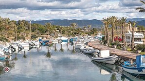 A marina with numerous boats docked along a waterfront, surrounded by palm trees and mountains in the background. - Stunning House Between the Countryside and the Sea - Southern Sardinia CIN: IT111070C2000U0960 (Porto Pino (Sardegna))