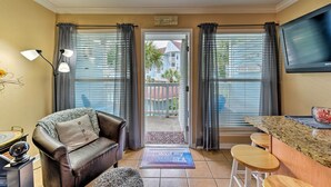 Ett vardagsrum med en brun lädersoffa, ett soffbord, en tv som är monterad på väggen och ett fönster med persienner.
