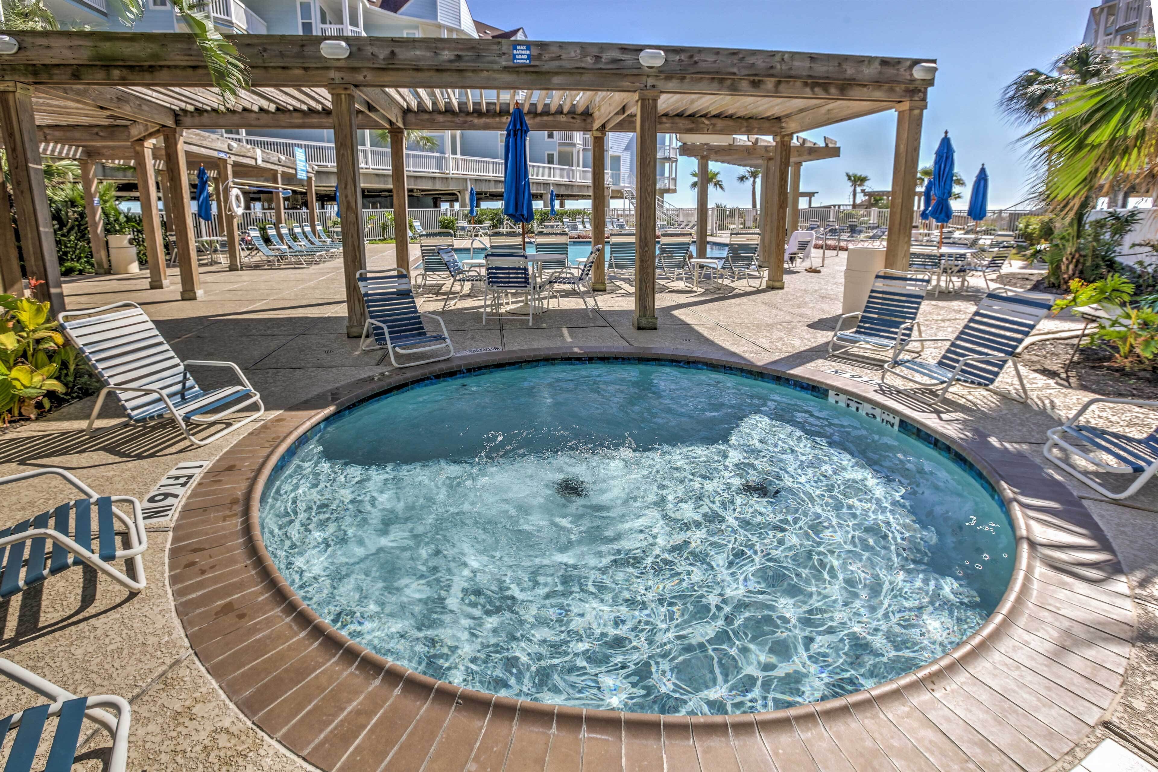 Een hottub omringd door ligstoelen en parasols, met een houten pergola erboven.