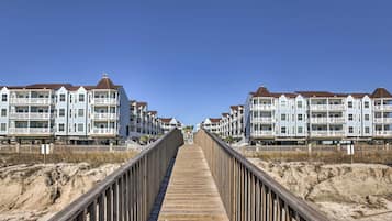 Een houten looppad dat leidt naar een rij strandappartementen met balkons.