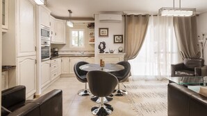 Eine moderne Küche mit weißen Schränken, ein Essbereich mit einem Glastisch und schwarzen Stühlen sowie ein Wohnbereich mit einer Ledersofa und einem Glastisch.