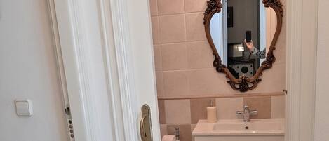 A bathroom with a white door, beige tiles, a mirror with an ornate frame, a sink, and a toilet.