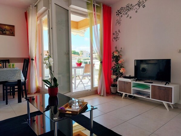 A living room with a glass table, a TV, and a balcony with a red chair.